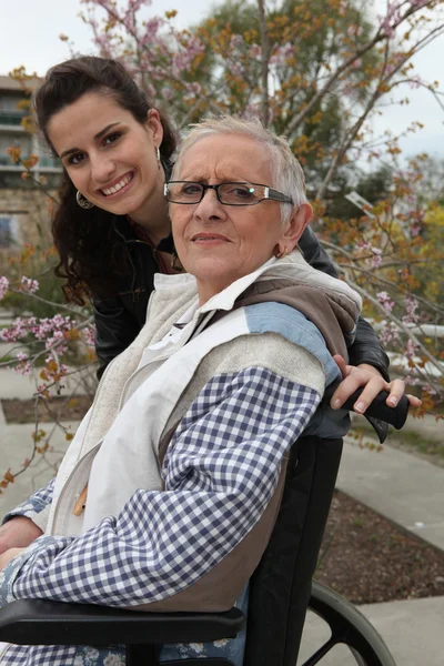 Junge Frau schubst eine ältere Dame im Rollstuhl — Stockfoto