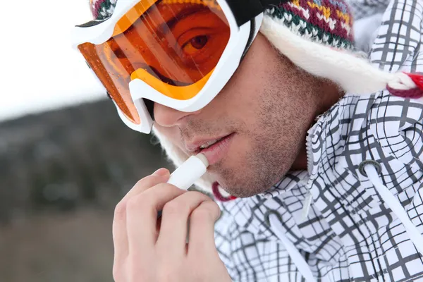 Unga skidåkare att sätta kall grädde lip pinnen på hans läppar — Stockfoto