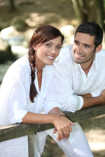 Couple in white leaning on a wooden fence — Stock Photo, Image