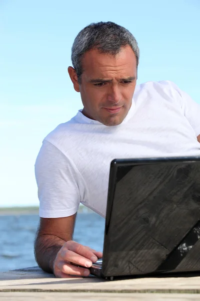 Homem usando seu laptop junto ao oceano — Fotografia de Stock