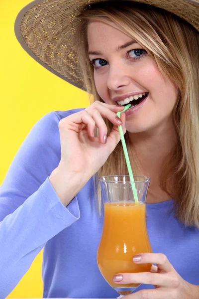 Atractiva rubia en sombrero de paja bebiendo jugo de naranja a través de paja — Foto de Stock