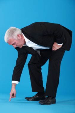 Mature businessman pointing et something on floor clipart