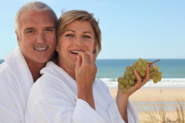 Couple eating grapes for breakfast on the beach clipart