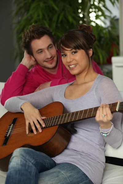 Pareja joven tocando una guitarra en casa — Foto de Stock