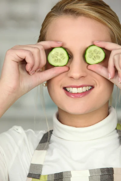 Blonde wearing apron hiding eyes with cucumber slices — Stock Photo, Image