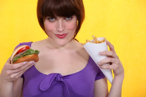 Mujer comiendo hamburguesa y papas fritas — Foto de Stock
