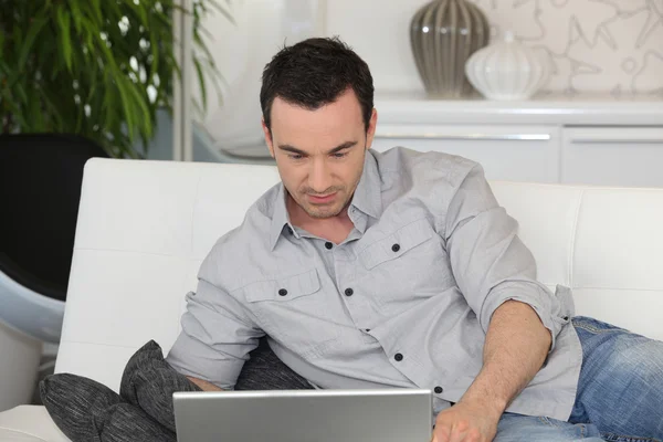 男人在沙发上使用一台笔记本电脑 — 图库照片