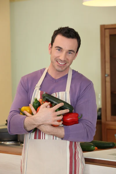 Uomo felice con grembiule contenente verdure — Foto Stock