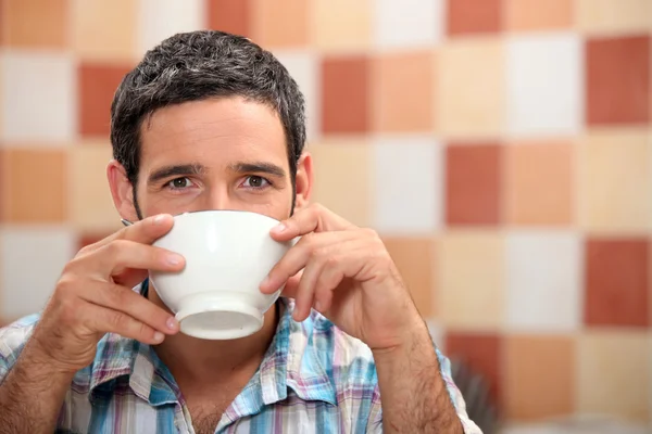 Homem bebendo de uma tigela branca em uma cozinha de azulejos — Fotografia de Stock