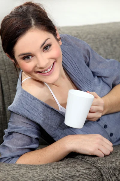 Красива дівчина з коричневим волоссям з чашкою на дивані — стокове фото