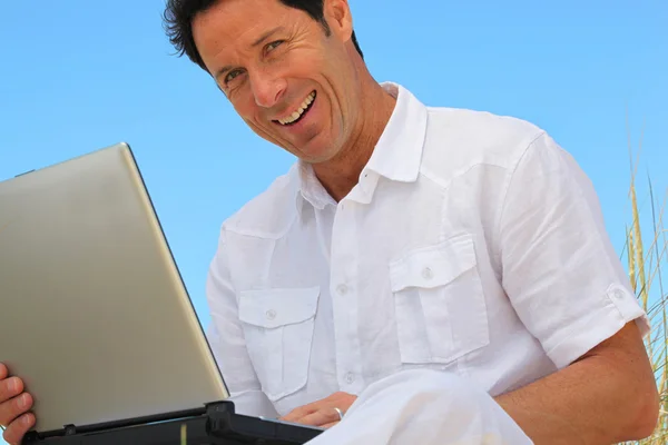 Άνθρωπος που είναι χαμογελώντας σε φορητό υπολογιστή στο γαλάζιο του ουρανού — Φωτογραφία Αρχείου