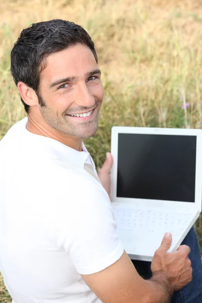 Homme souriant utilisant un ordinateur portable avec un écran vide dans un champ — Photo