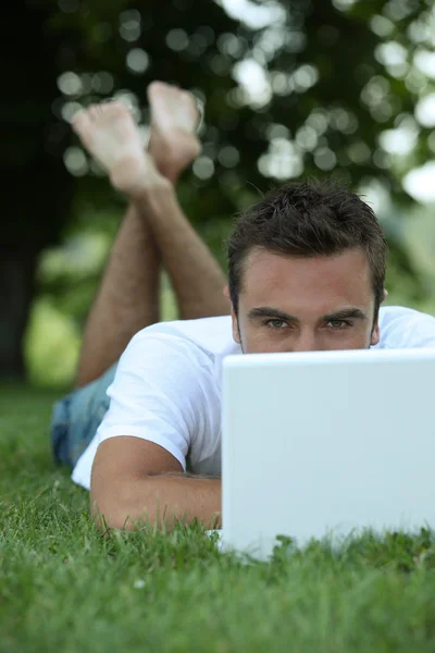Mann liegt im Gras vor Laptop — Stockfoto