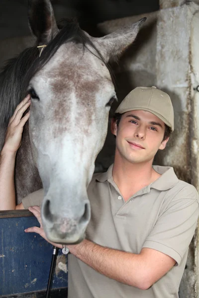 Молодой человек и лошадь в конюшне — стоковое фото