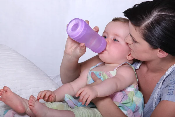Jovem mãe dando a seu bebê uma garrafa de bebidas — Fotografia de Stock