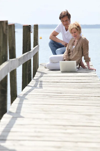 Äldre par med laptop sitter på ponton — Stockfoto
