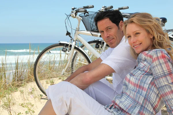 Couple with bikes sitting on the sand dunes — Stock Photo, Image