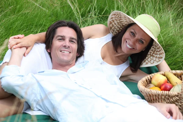 Couple lying on the grass with a basket of fruits — Stock Photo, Image