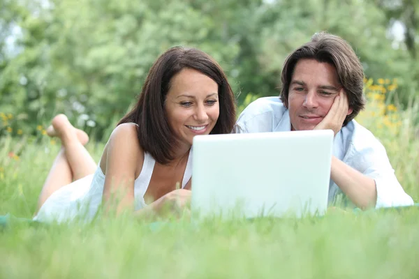 ラップトップ コンピューターの画面を見ながら草の上に横たわるカップル — ストック写真