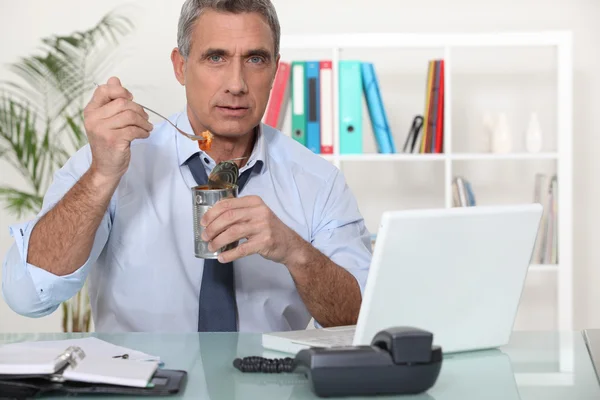 Trabalhador de escritório comendo uma lata de raviolis — Fotografia de Stock