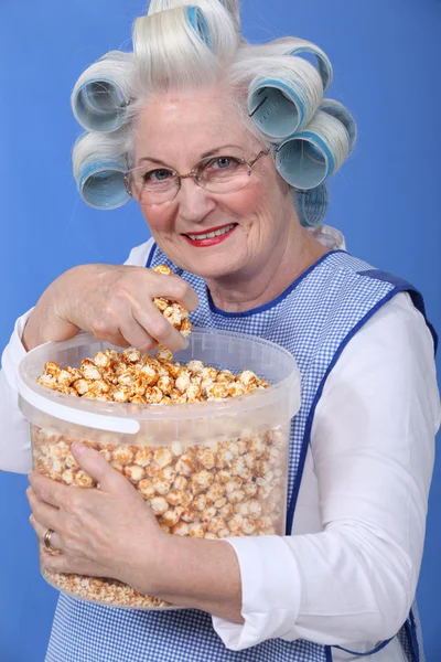 Seniorin mit Lockenwickler auf dem Kopf isst Popcorn — Stockfoto