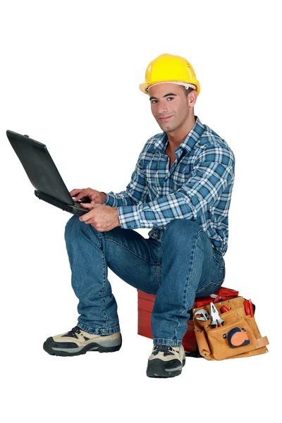 匠人坐在他的工具箱和使用他的笔记本电脑 — 图库照片
