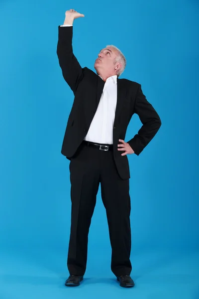 Ώριμος άνδρας σε κοστούμι που αγγίζουν την οροφή μπλε φόντο — Φωτογραφία Αρχείου