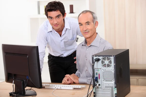 Een jonge man en een senior man achter een computer — Stockfoto