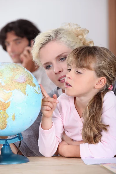 A mother is showing to her daughter some country on a globe, her husband is — Stock Photo, Image