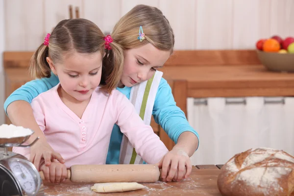 Sisters using rolling pin to roll dough — Stock Photo, Image