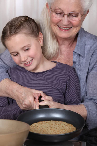 Girl and her granny cooking pancakes — Stock Photo, Image