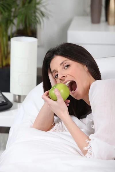 Donna sdraiata sul divano mangiare mela — Foto Stock