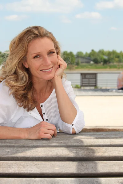Ahşap bir bankta oturan gülümseyen bir yazlık kadın portresi — Stok fotoğraf