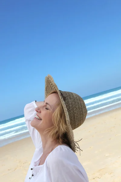 Woman walking along beach wearing straw hat — Stock Photo, Image