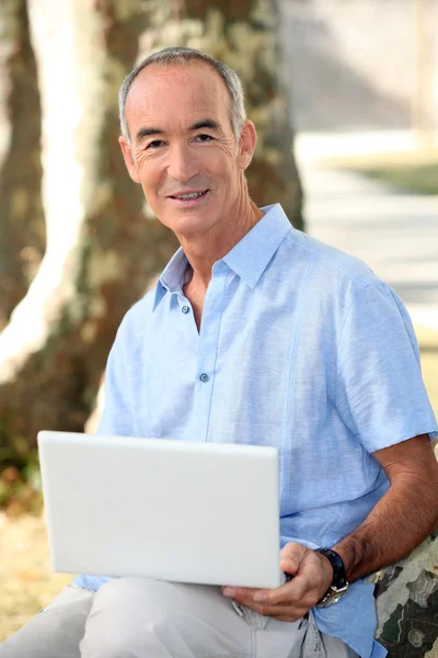 ラップトップ コンピューターを持つ公園で灰色の髪の男 — ストック写真