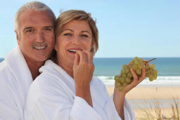 Pareja comiendo uvas para desayunar en la playa — Foto de Stock