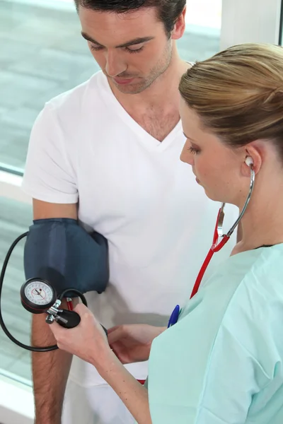 Молодая медсестра измеряет давление мужчины — стоковое фото