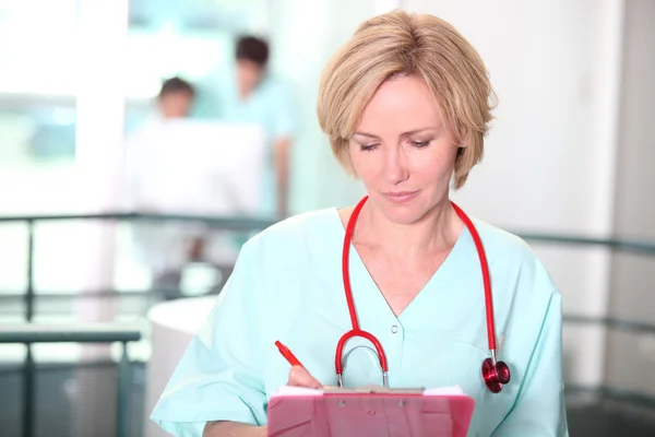A female doctor taking notes on a clipboard in the middle of a big room. — Stock Photo, Image