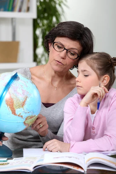 Moeder bedrijf een wereldbol en uitleg te geven aan haar dochter Stockafbeelding