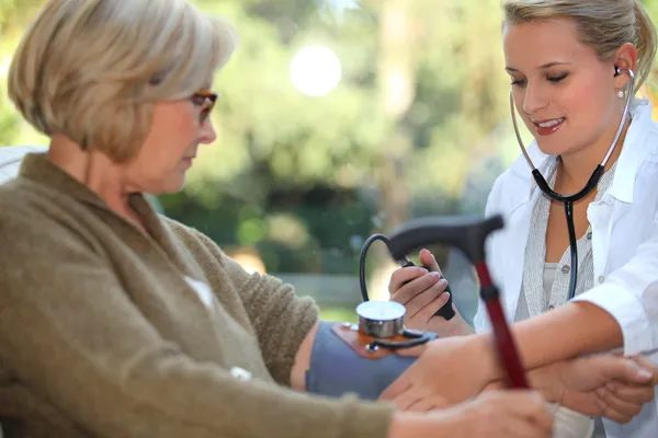 Verpleegkundige is het controleren van oude vrouw bloeddruk — Stockfoto