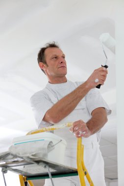 Man standing on a ladder and painting a wall clipart