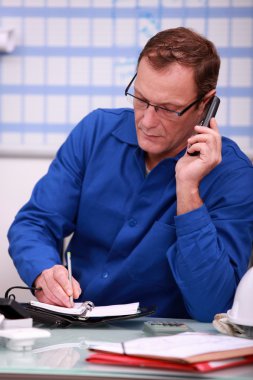 Man in blue overalls speaking on telephone clipart