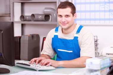 Young plumber in an office working on a computer clipart