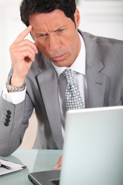 Businessman with a puzzled expression looking at a computer screen clipart