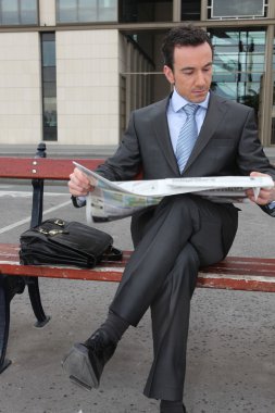 Businessman reading a newspaper on a bench clipart