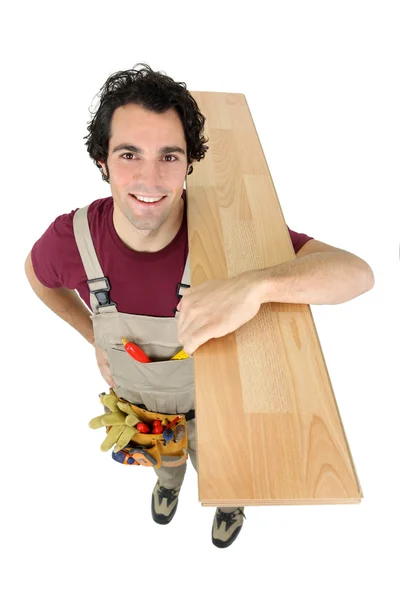 Feliz carpintero portando tablón de pie aislado sobre fondo blanco — Foto de Stock