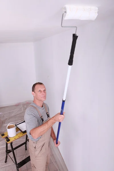 Decoratore utilizzando un'estensione a rulli per dipingere un soffitto bianco — Foto Stock