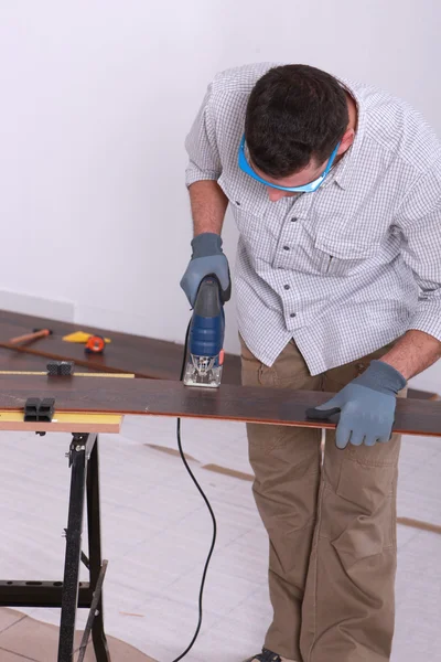 Uomo che usa un puzzle elettrico per tagliare un pezzo di pavimento in legno — Foto Stock