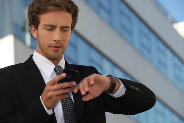 Město podnikatel kontrola hodinky a jeho telefon — Stock fotografie