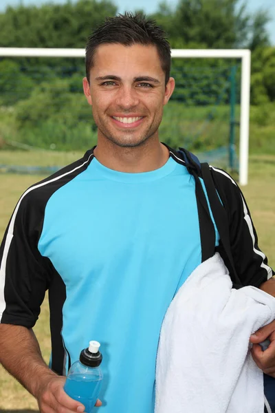 Uomo in piedi sul campo da calcio con bevanda energetica e asciugamano — Foto Stock